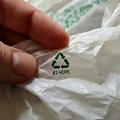 Close-up of a hand pointing at the recycling symbol on a crumpled plastic bag.